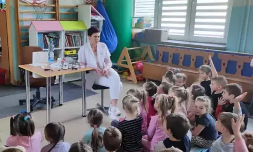 pani pielęgniarka siedzi przy stoliku przed nią na dywanie siedzi grupa dzieci