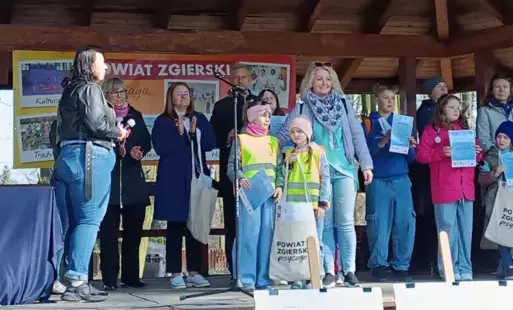 dzieci i dorośli stoją na podwyższonej scenie w tle pan prezydent miasta Zgierza