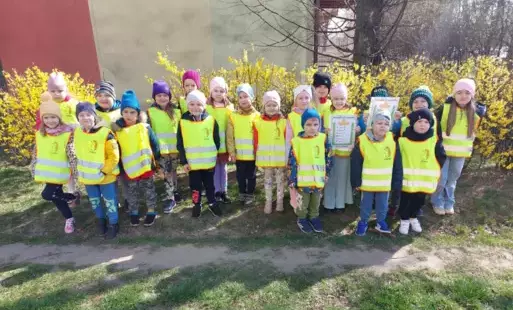 grupa dzieci pozuje do zdjęcia dzieci w kamizelkach odblaskowych w tle kwitnąca forsycja