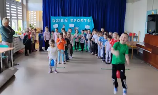 dzieci stoją w dwóch rzędach dzieci stojące na początku trzymają piłkę między kolanami