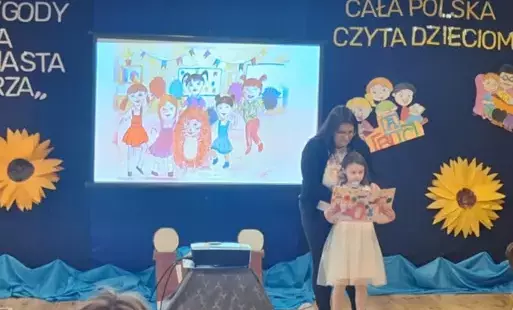 dziewczynka trzyma otworzoną książkę za nią pani nauczycielka w tle napi cała polska czyta dzieciom oraz obrazki dzieci