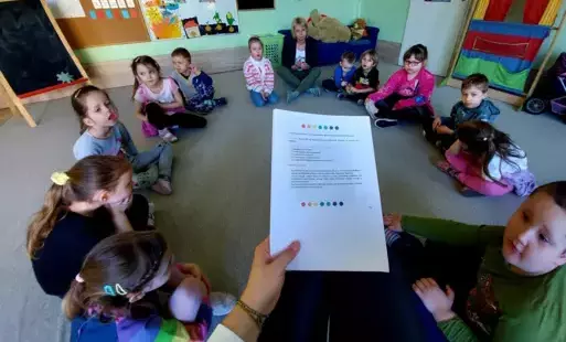 dzieci siedzą w kole przed nimi pani z kartką