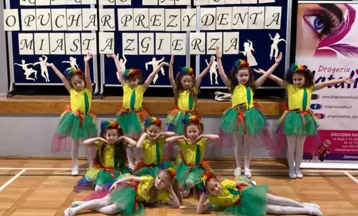 dziewczynki w żółtych koszulkach i kolorowych tiulowych spódnicach pozują do zdjęcia na tle napisu konkurs taneczny o puchar prezydenta miasta Zgierza
