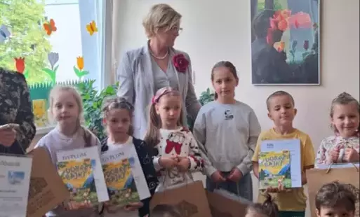 grupa dzieci pozuje do zdjęcia niektóre dzieci trzymają dyplomy w tle elegancko ubrana pani