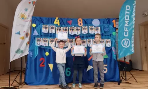 troje dzieci z dyplomami w rękach stoi na tle dekoracji z napiecem olimpiada matematyczna