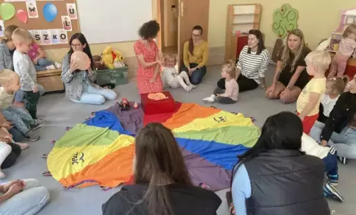 pani nauczycielka wraz z dziećmi i rodzicami siedzą dookoła chusty animacyjnej