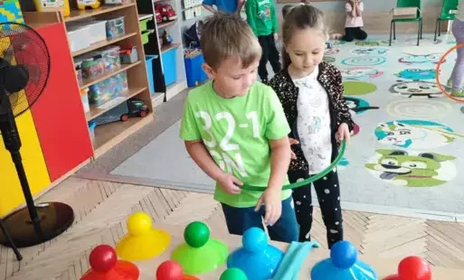 dziewczynka i chłopiec stoją przy stoliku z kolorowymi piłeczkami na stojakach