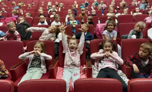 dzieci siedzą na dużej sali teatralnej obok siebie na bordowych fotelach