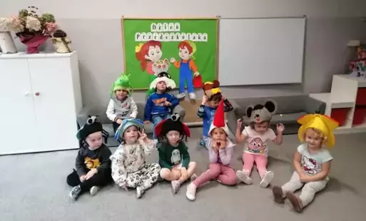 dzieci pozują do zdjęcia na tle dekoracji dzień przedszkolaka dzieci mają na głowach czapki w różnych kształtach kwiatek, biedronka itp