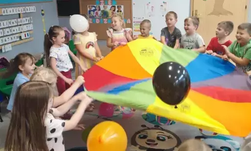 dzieci trzymają dookoła chustę animacyjną i podrzucają na niej balony