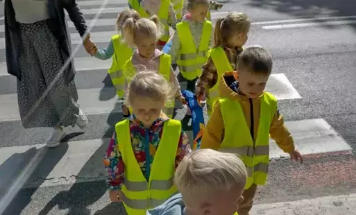 dzieci w odblaskowych kamizelkach przechodzą przez ulicę po pasach obok i z tyłu grupy idą panie