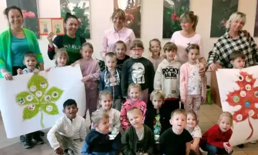 grupa dzieci wraz z paniami pozują do grupowego zdjęcia bo lewej i prawej stronie dzieci trzymają wielkie plakaty na których są dwa duże liście a na nich kropki pokolorowane przez dzieci w jesienne wzory