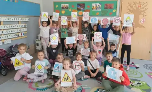 dzieci w klasie pozują do zdjęcia grupowego dzieci trzymają obrazki różnych znaków drogowych