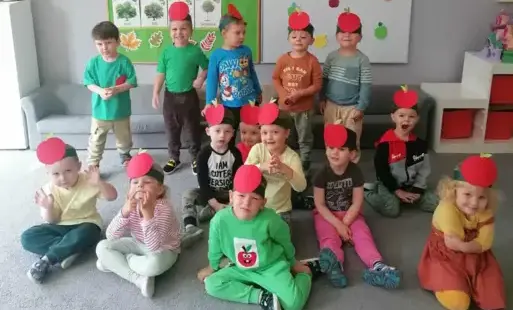 grupa dzieci w opaskach z obrazkiem jabłka pozuje do zdjęcia grupowego w tle dekoracja z jabłkami