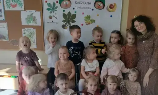 dzieci wraz z nauczycielką pozują do zdjęcia, w tle widać dekorację dzień kasztana