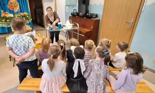nauczycielka stpi przed stolikiem z różnymi naczyniami dzieci przyglądają się co pani robi