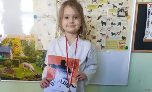 dziewczynka ubrana w kimono prezentuje dyplom i medal