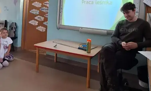 pan w stroju leśnika siedzi na krześle w tle tablica multimedialna na której widnieje napis 