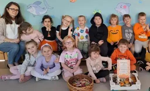 grupa dzieci wraz z panią pozuje do zdjęcia przed nimi stoi koszyk z cukierkami pudełko z donatami i dyplom