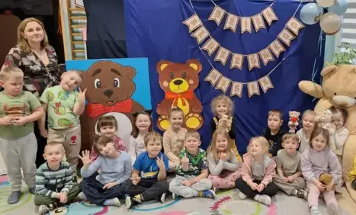 dzieci wraz z panią pozują do zdjęcia grupowego na tle dekoracji dzień pluszowego misia