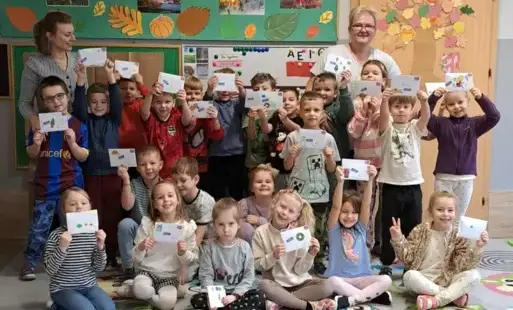 Grupa dzieci pozuje do zdjęcia grupowego dzieci trzymają w rękach listy z prawej i lewej strony stoją panie