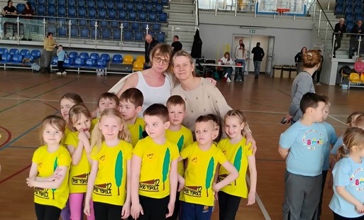 dzieci w koszulkach sportowych z logo przedszkola pozują do zdjęcia grupowego z paniami