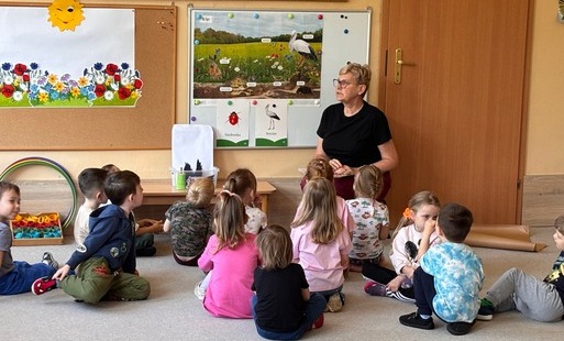 pani siedzi pod tablicą przed nią na dywanie siedzą dzieci w tle tablice z elementami o tematyce wiosennej