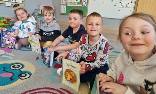 dzieci siedzą na dywanie trzymają książki