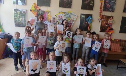 dzieci wraz z panią pozują do zdjęcia grupowego w dłoniach trzymają rysunki swoich tatusiów