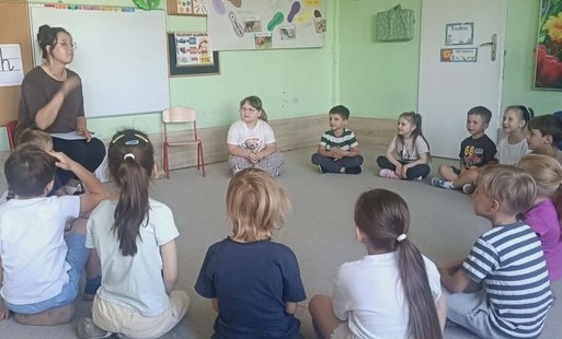 pani siedzi na stołeczku adzieci w kole na dywanie