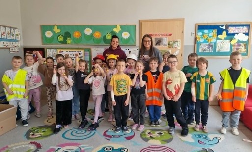 dzieci wraz z dwiema paniami pozują do zdjęcia grupowego niektóre dzieci mają na sobie kamizelki odblaskowe a inne kaski