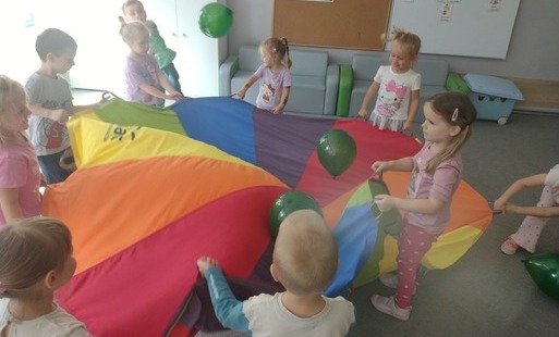 dzieci trzymają chustę animacyjną nad którą unoszą się kolorowe balony